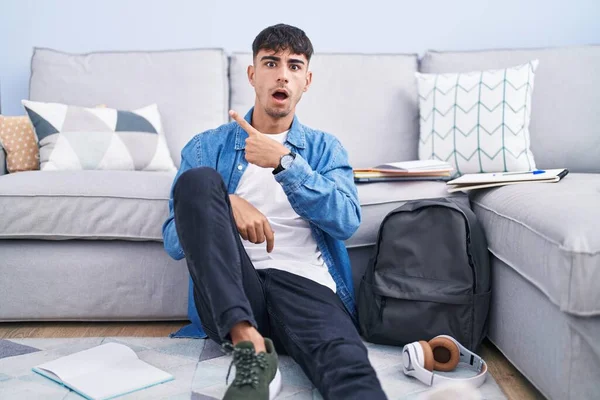 Young Hispanic Man Sitting Floor Studying University Surprised Pointing Finger — Zdjęcie stockowe