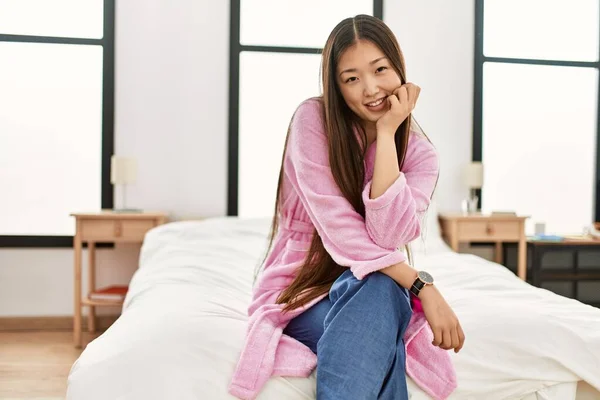 Young chinese girl smiling happy sitting on the bed at bedroom.
