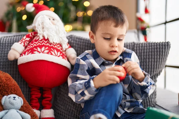 可爱的幼儿抱着装饰球坐在家里圣诞树旁的沙发上 — 图库照片