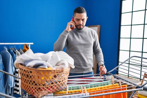 Young Latin Man Talking Smartphone Hanging Clothes Clothesline Laundry Room — Stockfoto