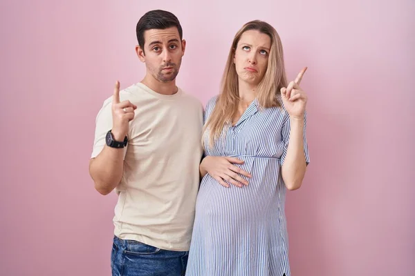 Casal Jovem Esperando Bebê Sobre Fundo Rosa Apontando Para Cima — Fotografia de Stock