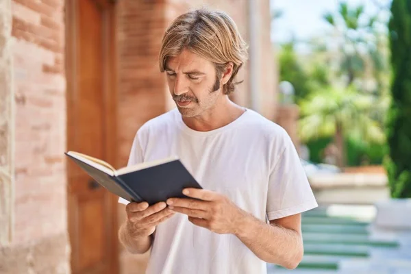 Young blond man smiling confident reading book at street