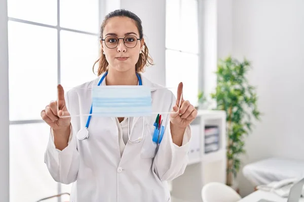 Young Hispanic Doctor Woman Holding Safety Mask Puffing Cheeks Funny — Stockfoto