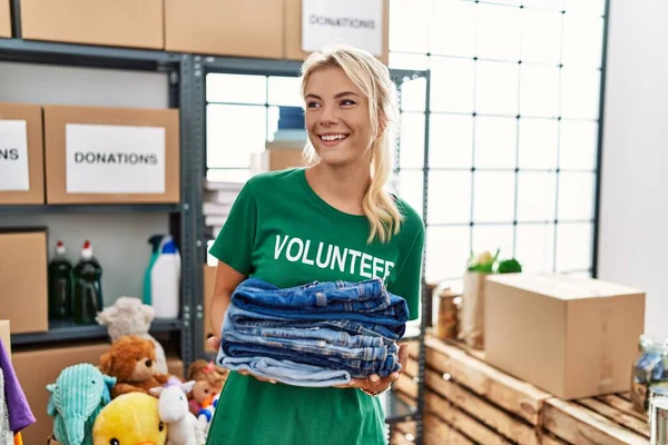 Young Blonde Volunteer Girl Smiling Happy Holding Stack Folded Jeans — Stock Photo, Image