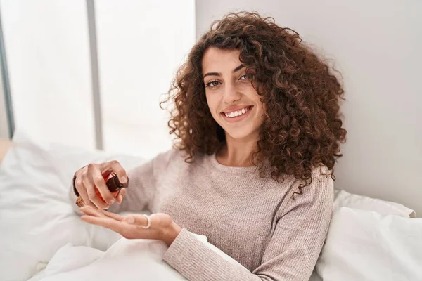 Young Hispanic Woman Pouring Lotion Hand Sitting Bed Bedroom — Stockfoto