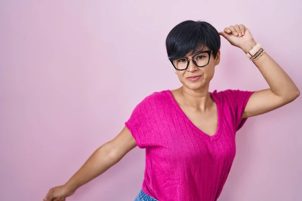 Young asian woman with short hair standing over pink background dancing happy and cheerful, smiling moving casual and confident listening to music