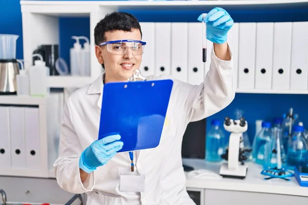 Young non binary man scientist reading report holding blood test tube at laboratory