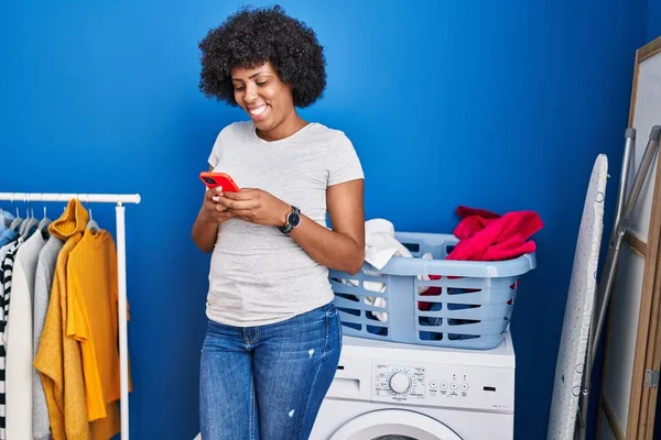 在洗衣房用智能手机等洗衣机的非洲裔美国女人 — 图库照片