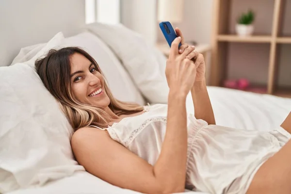 使用智能手机的年轻女子躺在床上 — 图库照片