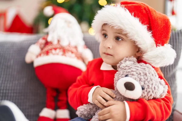 可爱的他惊慌失措的小孩抱着玩具熊坐在家里圣诞树旁的沙发上 — 图库照片