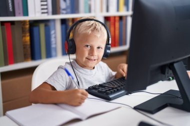 Adorable toddler student using computer writing on notebook at classroom