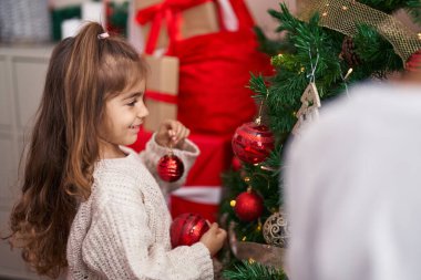 Tapılası İspanyol kız gülümseyerek evde kendine güvenen bir Noel ağacı süsler.