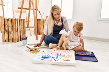 Mother and daughter smiling confident drawing sitting on floor at art studio