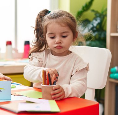 Anaokulunda masaya oturmuş kağıda resim çizen sevimli İspanyol kız öğrenci.