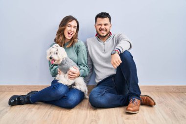 Young hispanic couple sitting on the floor with dog winking looking at the camera with sexy expression, cheerful and happy face. 