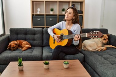 Genç İspanyol kadın klasik gitar çalıyor. Evde köpeklerle birlikte kanepede oturuyor.