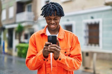 Sokakta akıllı telefon kullanan, kendinden emin gülümseyen Afrikalı Amerikalı bir adam.