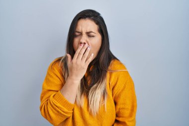 Tecrit edilmiş arka planda duran genç İspanyol kadın ağzıyla ağzını kapatmaktan sıkılmış. Huzursuz ve uykulu.. 