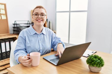 Young redhead woman working at the office using computer laptop with a happy and cool smile on face. lucky person. 