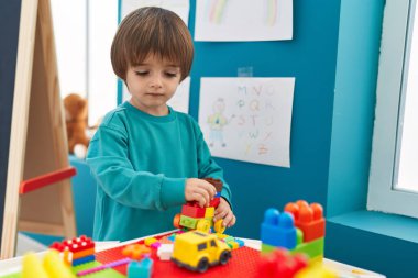 Adorable toddler playing with construction blocks standing at kindergarten