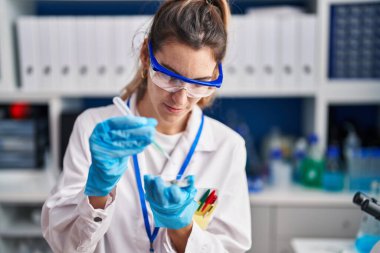Young woman scientist pouring liquid on sample at laboratory