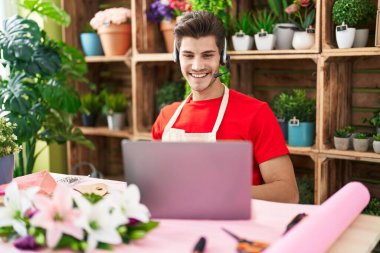 Çiçekçide çalışan İspanyol asıllı genç adam mutlu ve havalı bir gülümsemeyle video görüşmesi yapıyor. şanslı kişi. 