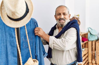 Giysi dükkanından kendine güvenen, gülümseyen yaşlı, kır saçlı adam.