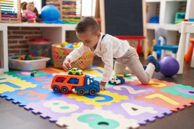 Adorable toddler playing with truck toy sitting on floor at kindergarten