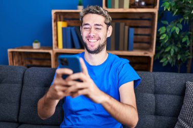 Genç adam evde koltukta oturan smartphone kullanarak