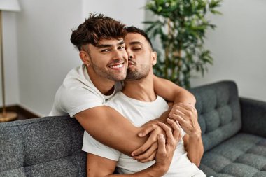 İki İspanyol erkek, kendilerine güvenerek gülümsüyor ve evde birbirlerine sarılıyorlar.