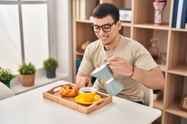 Genç adam kahvaltı yapıyor. Evde masada oturuyor.