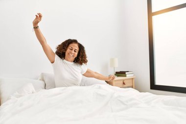 Orta yaşlı İspanyol kadın gülümseyerek yatak odasında kendine güvenerek uyanıyor.