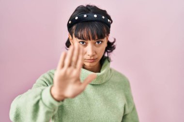 Young beautiful woman standing over pink background doing stop sing with palm of the hand. warning expression with negative and serious gesture on the face. 