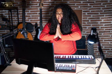 Plus size hispanic woman playing piano at music studio begging and praying with hands together with hope expression on face very emotional and worried. begging. 