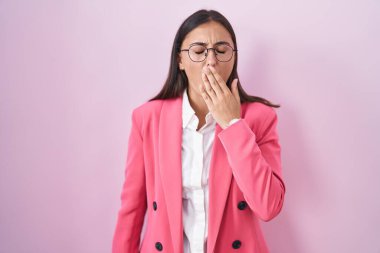 Young hispanic woman wearing business clothes and glasses bored yawning tired covering mouth with hand. restless and sleepiness. 