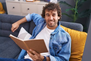 Evdeki kanepede oturmuş kitap okuyan genç bir İspanyol.