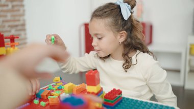 Adorable caucasian girl playing with construction blocks sitting on table at kindergarten