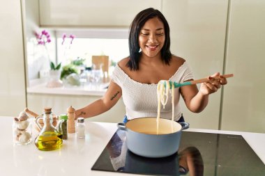 Hispanic brunette woman cooking spaghetti at the kitchen