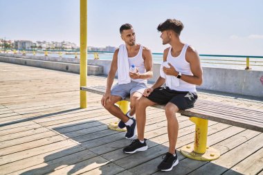 İki İspanyol erkek, gülümseyen bir çift, deniz kenarında bankta oturuyorlar.