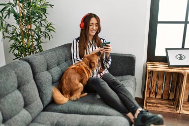 Genç İspanyol kadın akıllı telefon kullanıyor. Kanepede köpeğiyle oturuyor.