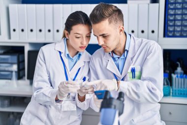 Man and woman scientists using smartphone looking sample at laboratory