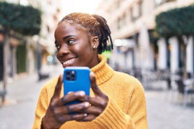 Afro-Amerikalı kadın sokakta akıllı telefon kullanarak kendine güveniyor.