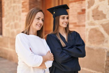 Two women mother and graduated daughter standing with arms crossed gesture at campus university