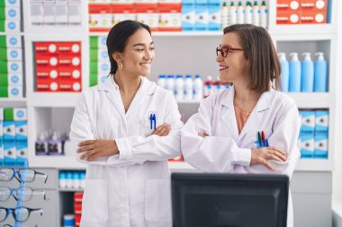 Two women pharmacist standing with arms crossed gesture at pharmacy