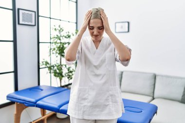 Young caucasian physiotherapy woman working at home suffering from headache desperate and stressed because pain and migraine. hands on head. 