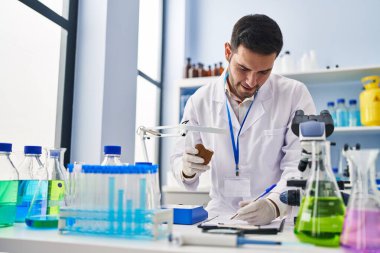 Genç İspanyol bilim adamı elinde değerli taşla laboratuardaki belgeye yazı yazıyor.