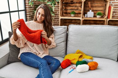 Young hispanic woman smiling confident holding handmade scarf at home