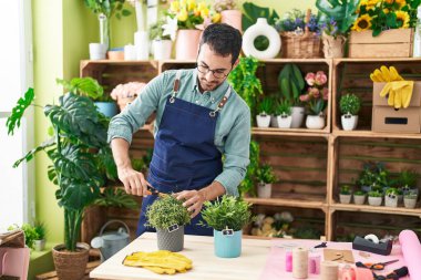 Young hispanic man florist cutting plant at flower shop