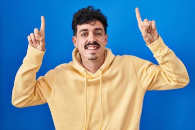 Mavi arka planda duran İspanyol adam şaşırmış, şaşırmış ve parmaklarıyla işaret ediyor ve kollarını kaldırıyordu.. 