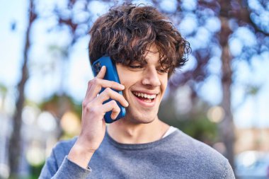 Genç İspanyol adam gülümsüyor. Parktaki akıllı telefondan konuşuyor.